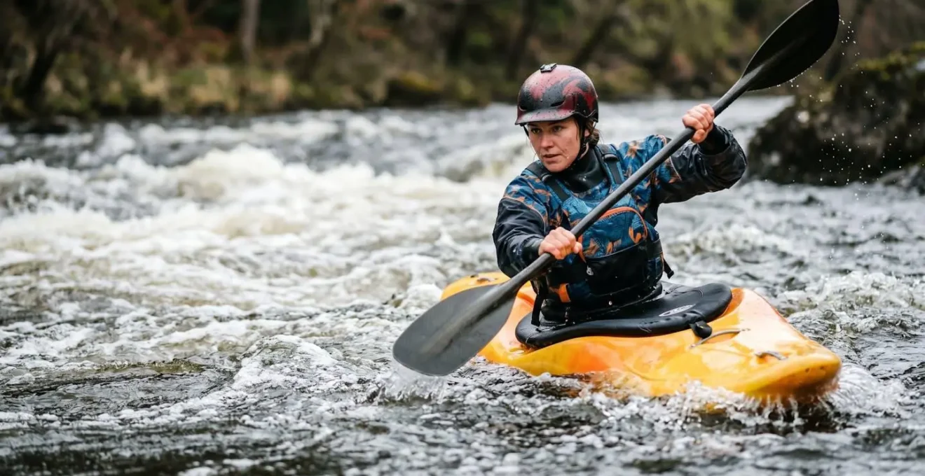Kayaker maneuvering through whitewater rapids with safety equipment and proper technique
