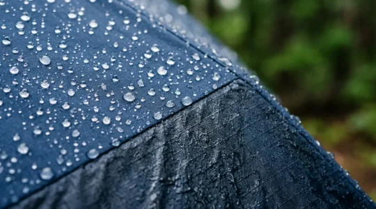 Detailed view of water droplets beading and failing on outdoor jacket fabric during heavy rain